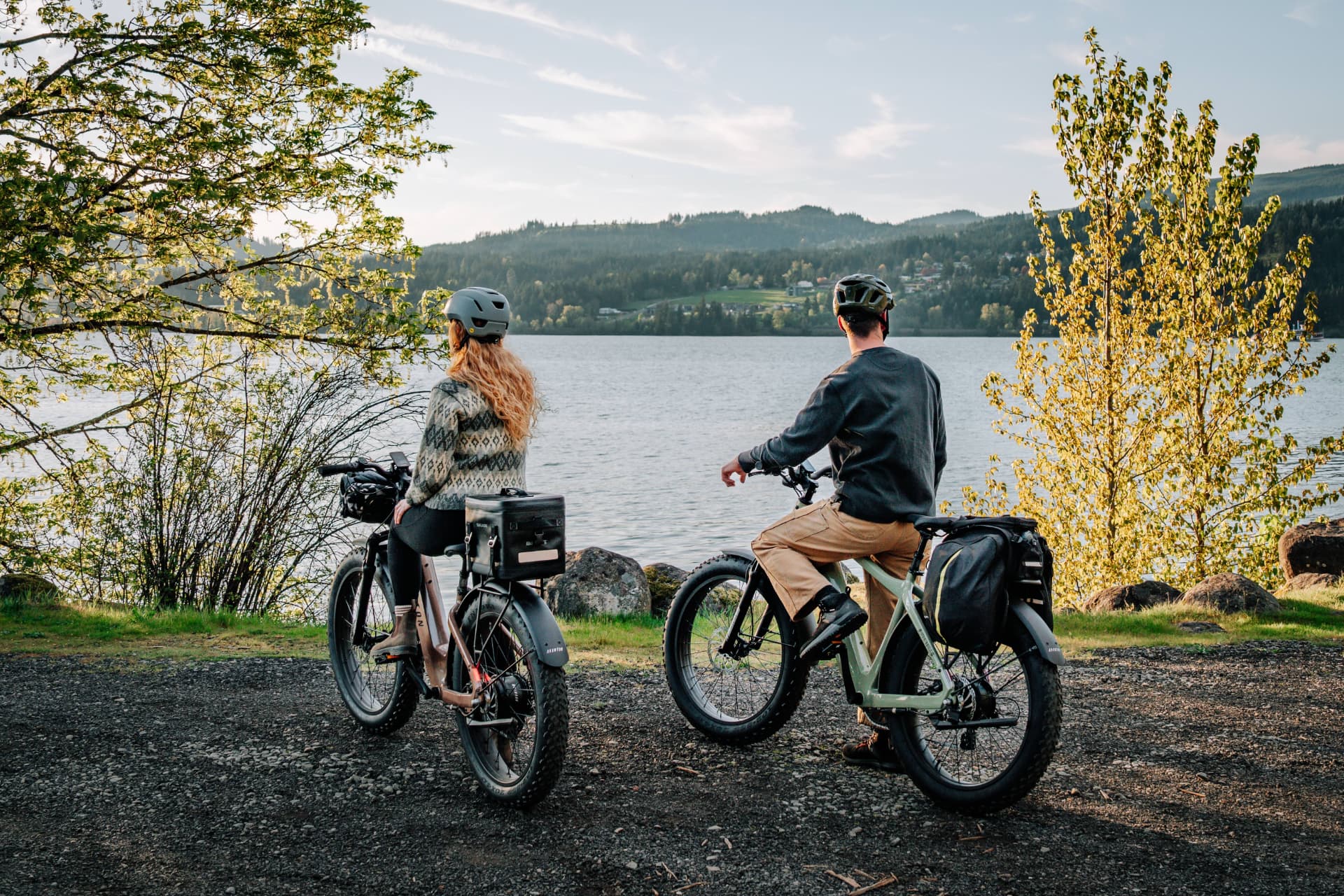 Dos ciclistas sobre bicicletas eléctricas Aventon mirando un lago rodeado de bosque