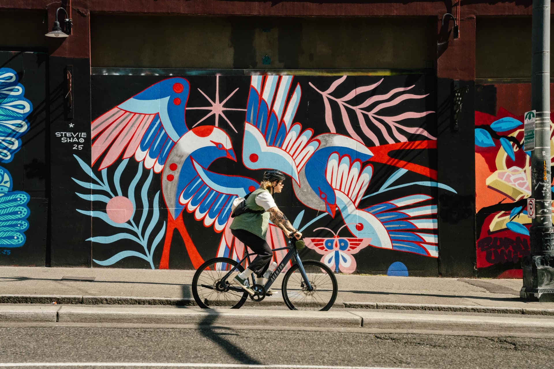 Persona pedaleando una bicicleta eléctrica Aventon frente a un mural urbano