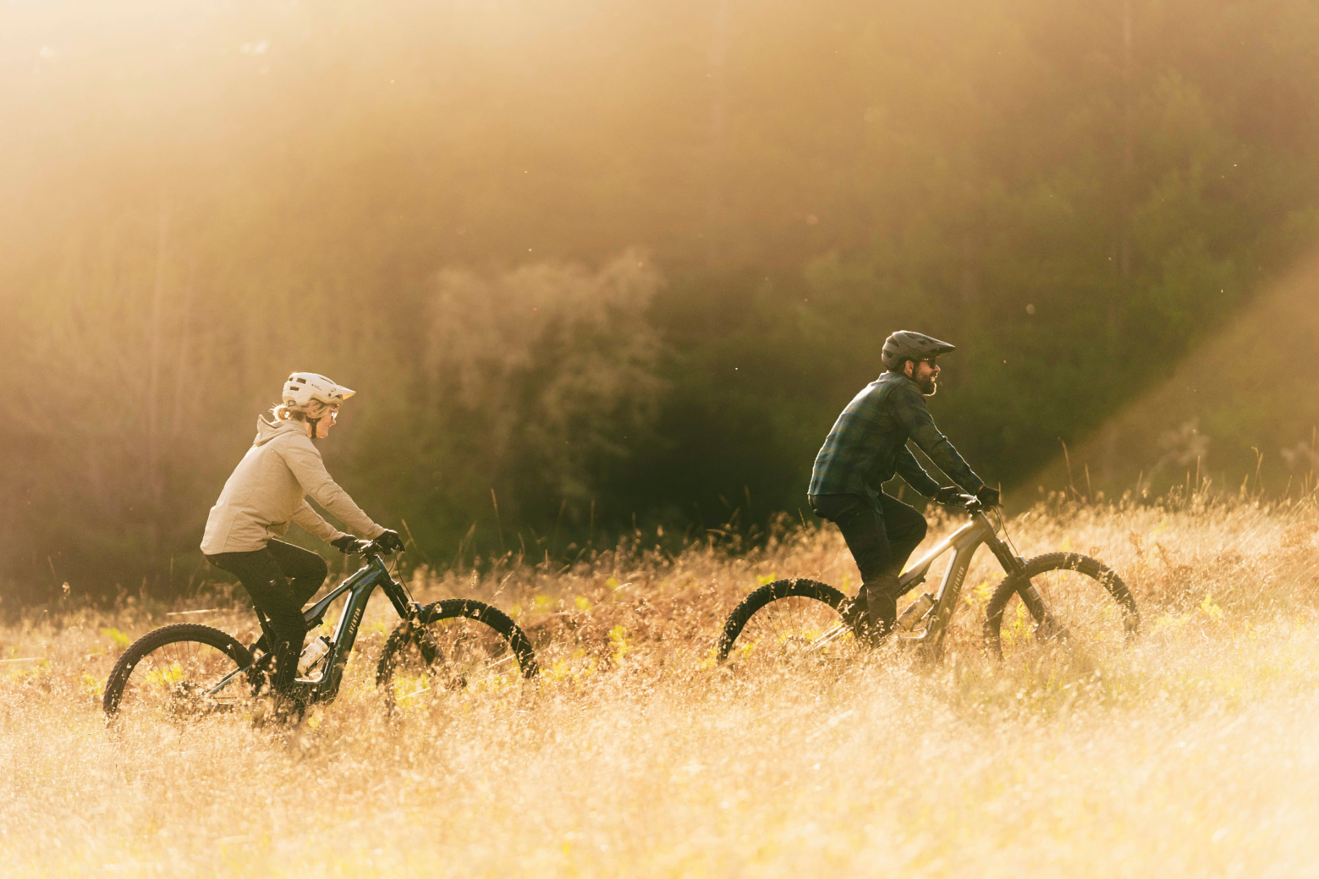 Dos ciclistas en un campo dorado al atardecer sobre bicicletas eléctricas Aventon Current ADV